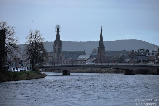 A bridge spanning over a river with buildings featuring steeples and spires in the background - image from year 2026 #043