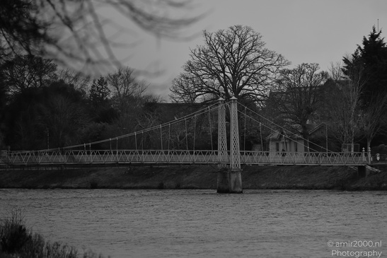 Scottish City Inverness a suspension bridge spans a calm river, surrounded by leafless trees and - image from year 2026 #044
