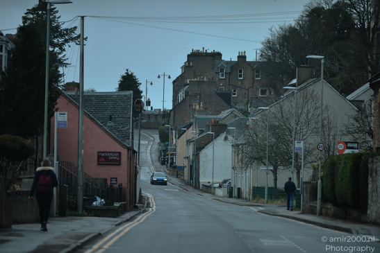 A quiet street in a Scottish town with a pink building and a person walking away. - image from year 2026 #045