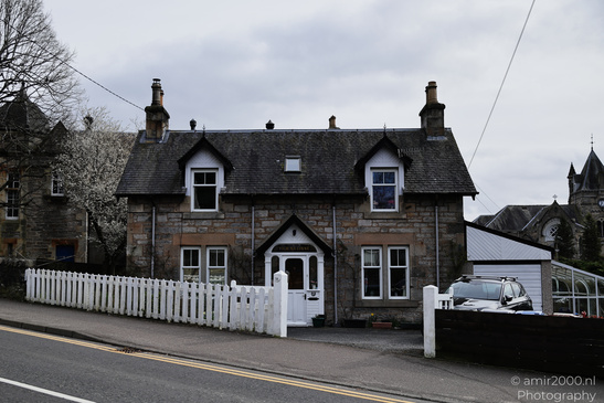 Town Pitlochry a quaint stone house with a white picket fence and a car parked in front. - image from year 2026 #007