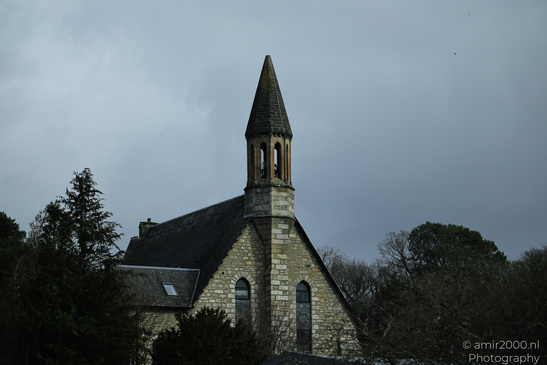 Town Pitlochry a quaint stone church with a pointed steeple stands amidst trees under an - image from year 2026 #011
