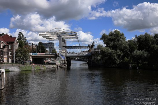 Willemsbrug Haarlemmerplein canal with a bridge and lush greenery on either side under a partly - image from year 2026 #001