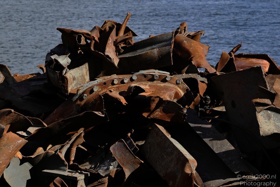 Rusted metal debris lies on a rocky shore with the ocean. - image from year 2026 #001