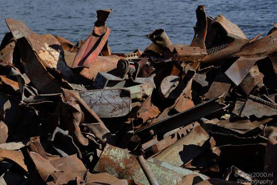 A pile of rusted metal debris with various shapes and sizes scattered on land near water in - image from year 2026 #003