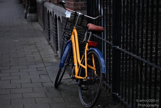 a close up of an orange bike with red seat against a dark railing. image from year 2026 #1