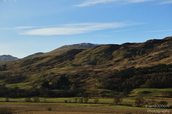 A landscape with rolling hills covered partially in snow and grass, surrounded by trees and - image from year 2026 #002