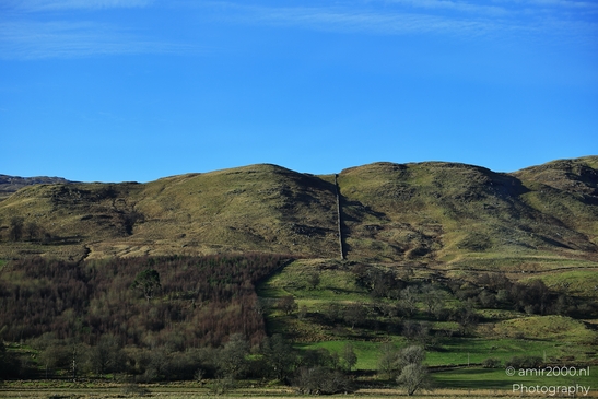 A landscape with rolling hills covered in green vegetation under a clear blue sky in Scotland - image from year 2026 #003