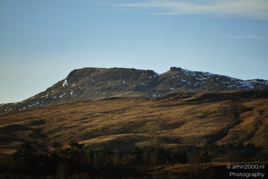 A mountainous landscape with patches of snow on its peaks and slopes covered in dry grass under - image from year 2026 #004