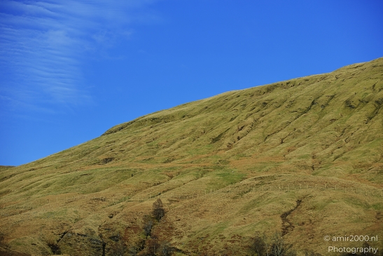 A grassy hill under a clear blue sky with some scattered clouds in Scotland United Kingdom. - image from year 2026 #013