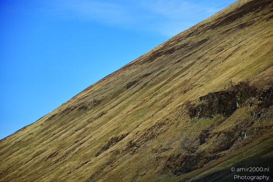 A steep hillside covered with dry grass and patches of bare earth under a clear blue sky in - image from year 2026 #015