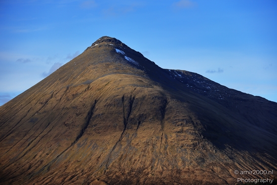 A mountain with rugged terrain and sparse vegetation under a clear blue sky in Scotland United - image from year 2026 #018