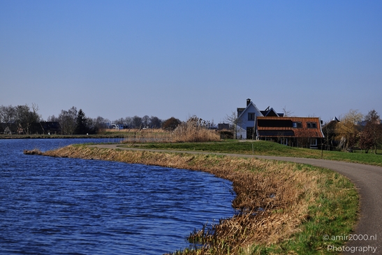 A serene riverside scene with a house featuring a distinctive orange-tiled roof situated on a - image from year 2026 #007