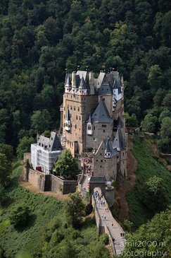 A medieval castle perched on a rocky hill, surrounded by lush greenery and visitors walking - image from year 2026 #001