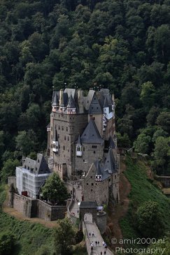 A medieval castle perched on a rocky hill, surrounded by lush greenery and visitors walking - image from year 2026 #010