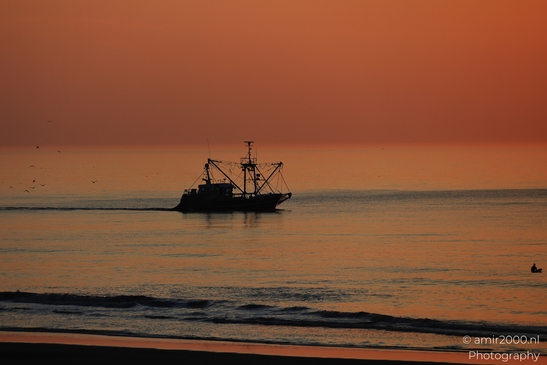 A fishing boat sails on the calm waters of the North Sea at sunset, with a distant figure in the - image from year 2026 #003