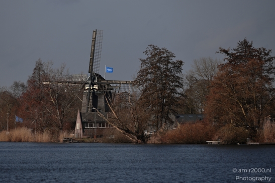 A traditional windmill with a blue flag stands beside a body of water in Driemond, Netherlands. - image from year 2026 #001
