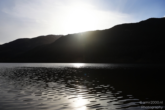 A body of water with ripples reflecting sunlight, silhouetted mountains in the background, and a - image from year 2026 #003