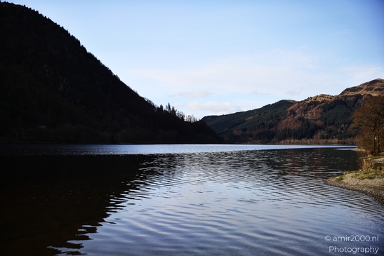 A serene lake surrounded by forested hills under a partly cloudy sky in Scotland United Kingdom. - image from year 2026 #004