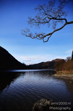 A serene lakeside scene under a clear blue sky with scattered clouds in Scotland United Kingdom. - image from year 2026 #006