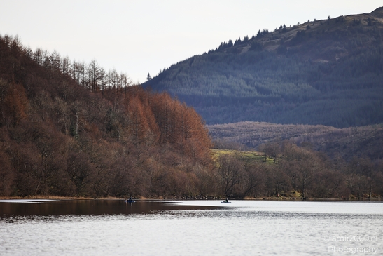 Two individuals paddling on a calm lake surrounded by autumnal trees and a forested hillside - image from year 2026 #007