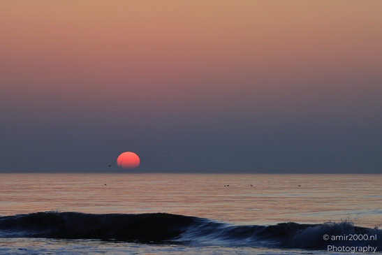 A sunset over the North Sea, with a large, reddish sun setting behind the horizon, casting a - image from year 2026 #019