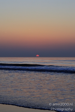 A sunset over the North Sea, with the sun setting near the horizon and gentle waves lapping at - image from year 2026 #022