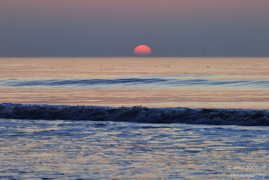 A sunset over the North Sea, with the sun setting low on the horizon and gentle waves lapping - image from year 2026 #023