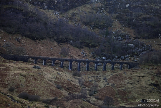 A stone viaduct with multiple arches spanning across a valley surrounded by rugged hills and - image from year 2026 #016