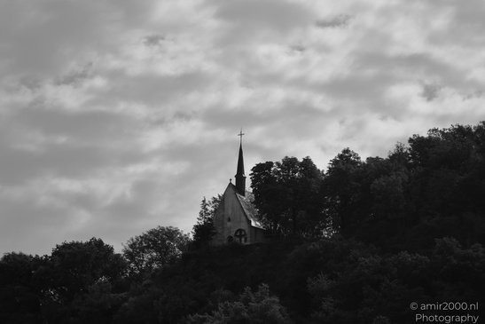 Stone Castle Structures: A solitary church spire rises above a dense forest under a cloudy sky - image from year 2026 #002