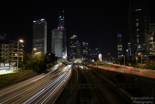 A nighttime cityscape with several prominent skyscrapers illuminated against the dark sky in Tel - image from year 2026 #003