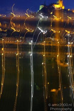 Light trails in the foreground with a cityscape and a body of water in the background at night. - image from year 2026 #001