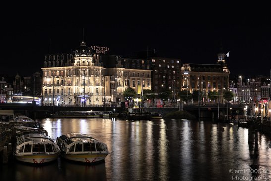 Buildings along the water, illuminated at night, with boats in the foreground in Amsterdam, - image from year 2026 #002