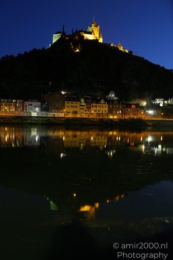 A nighttime scene of a castle perched atop a hill, with colorful buildings and a river in the - image from year 2026 #002