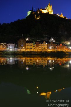 A nighttime scene of a castle perched atop a hill, with illuminated buildings and a river in the - image from year 2026 #003