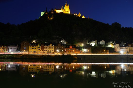 A nighttime view of a town with colorful buildings along a riverbank, illuminated by lights, and - image from year 2026 #004