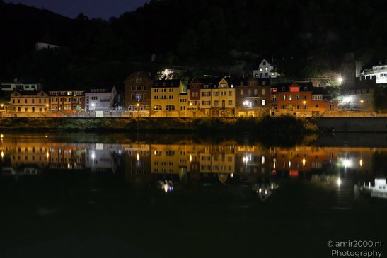 A row of buildings illuminated at night, reflected in a calm body of water in the foreground, - image from year 2026 #005