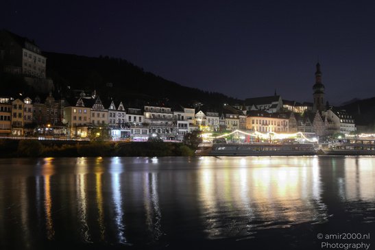 A river reflects the lights of a town at night, with buildings and a church steeple visible in - image from year 2026 #008