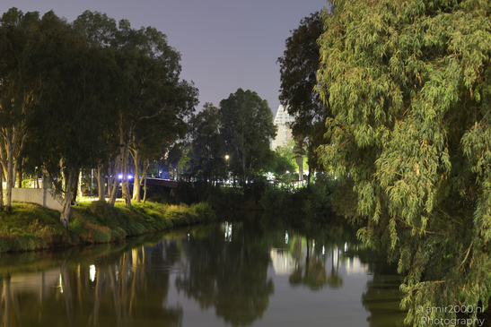 A calm river surrounded by trees and illuminated lights in the background under a twilight sky - image from year 2026 #003